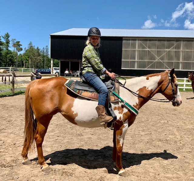 A smiling woman riding a brown horse